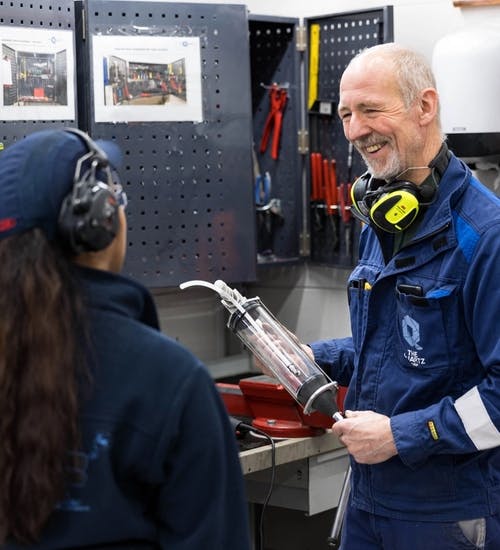 Older man holding a plastic device talking and smiling with a younger female colleague.