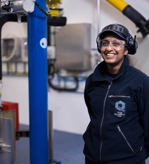 Young woman wearing hard hat, protective glasses and protective earwear standing in factory