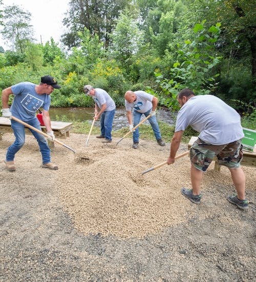 Group of men raking gravel into place by stream bank